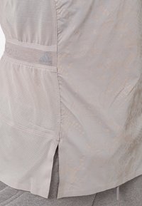 Lichtroze sporttop met een textuurpatroon, mesh zijpanelen en een elastische tailleband met een klein logo.