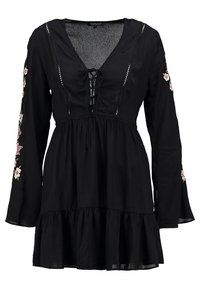 Svart långärmad klänning med v-utskärning, snörning framtill och blommig broderi på ärmarna; har en utsvängd kjol och lättviktsmaterial.