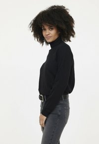 Pull à col roulé noir avec des manches longues, associé à un jean gris foncé. Présente une coupe décontractée et des poignets côtelés. Design simple, sans motifs.