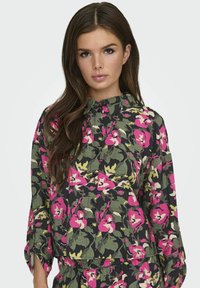 Blomstret skjorte med et sort, grønt og pink camouflagemønster, klassisk krave, knaplukning og lange ærmer.