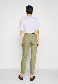 Camicetta a maniche corte di color lilla abbinata a pantaloni in verde oliva a vita alta. I pantaloni presentano tasche posteriori e un'etichetta nera del marchio.