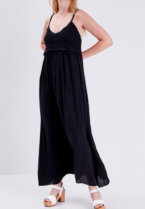 Robe maxi noire avec un corsage en crochet et des bretelles spaghetti ajustables, jupe fluide, portée avec des sandales plateformes blanches.