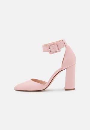 Zapato de tacón alto de cuero rosa con punta afilada, hebilla gruesa y correa de tobillo ancha con una hebilla cuadrada.