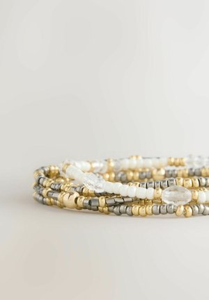 Multiple beaded bracelets featuring gold, silver, and white beads, with smooth and textured detailing and varying shapes, including oval and round.