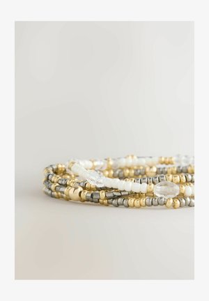 Multiple beaded bracelets featuring gold, silver, and white beads, with smooth and textured detailing and varying shapes, including oval and round.
