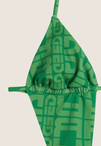 Vihreä bikinitoppi, valmistettu sileästä kankaasta, jossa on rohkea kuvio isoilla tekstikoristeilla, rypytetty yksityiskohta alaosassa ja ohuet säädettävät olkaimet.