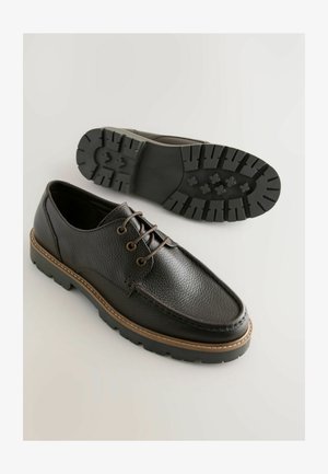 Scarpe in pelle nera con una finitura strutturata, dotate di due passanti, accenti marroni e una suola in gomma robusta con un motivo di battistrada.