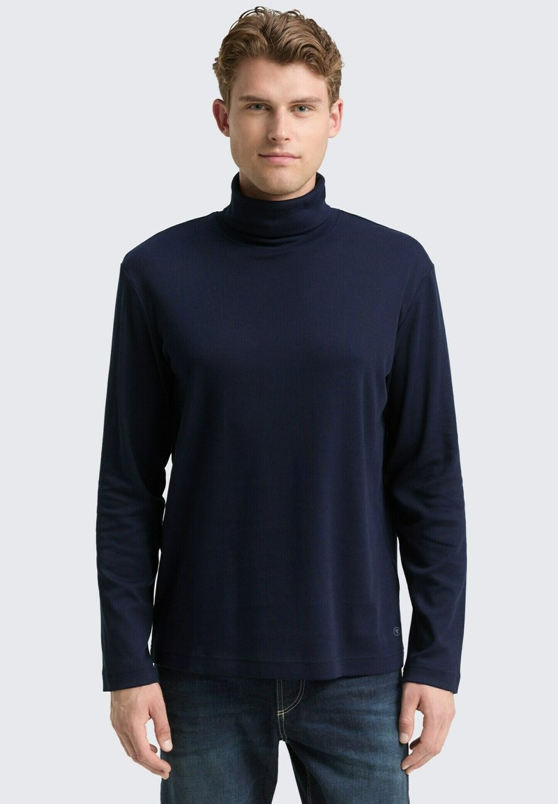 Marineblauer Rollkragenpullover mit langen Ärmeln, weichem geripptem Material, geradem Schnitt, kombiniert mit blauen Jeans. Einfaches Design, keine sichtbaren Muster.