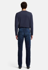 Jeans in denim blu scuro con vestibilità a gamba dritta, caratterizzati da due tasche posteriori e sottili dettagli di cucitura. Abbinati a una maglia a maniche lunghe color navy.