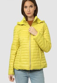 Chaqueta acolchada amarilla con capucha de piel sintética. Cuenta con cierre de cremallera y bolsillos laterales. Acabado texturizado con costuras horizontales.