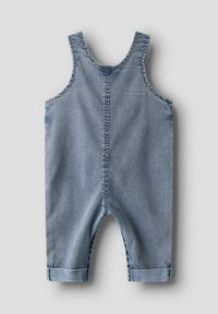 Combinaison bébé en denim bleu clair, sans manches, avec larges bretelles, couture centrale et pantalons retroussés sur fond uni.