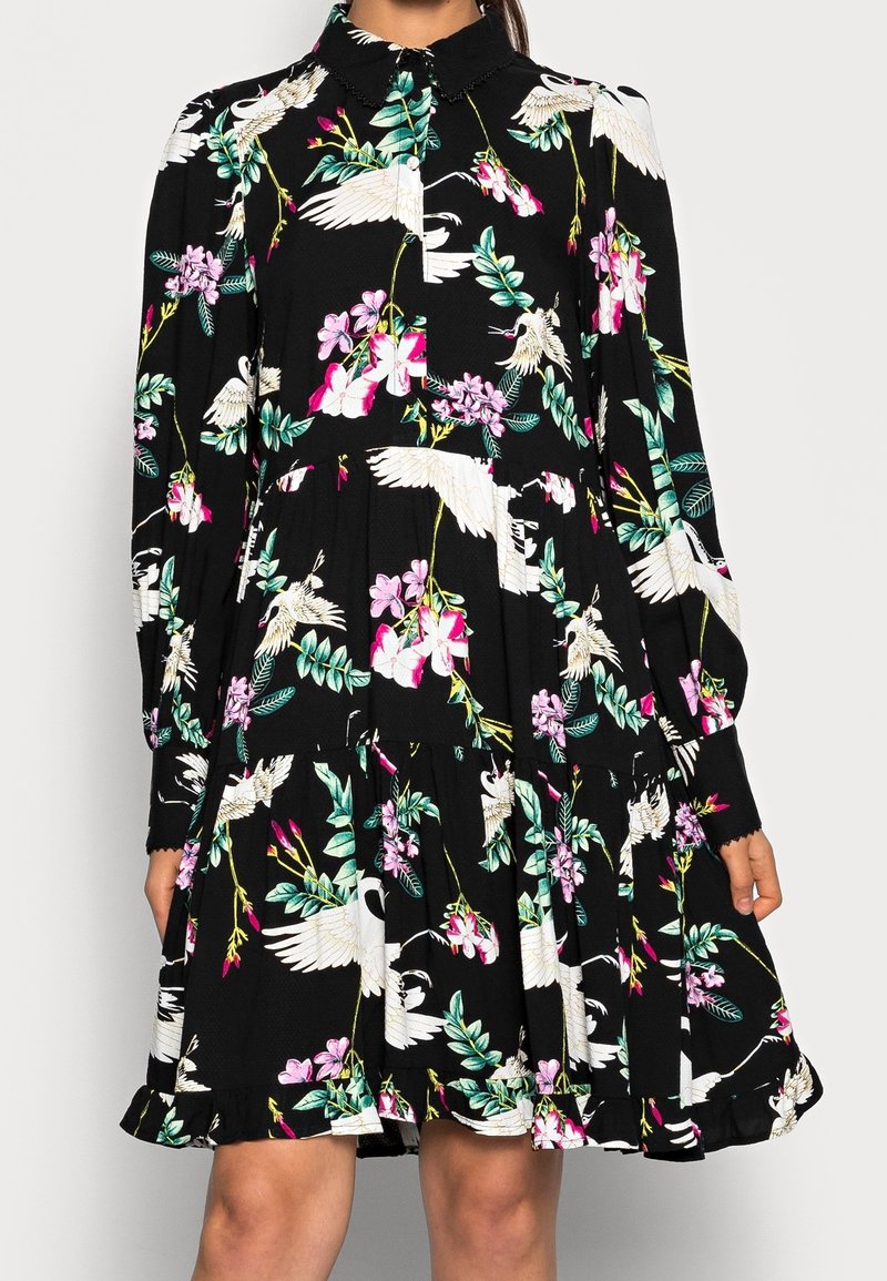 Robe noire à manches longues avec un motif floral et de grues blanches, boutonnée à l'avant, jupe à étages et col classique.