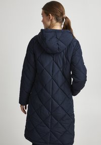 Navy quilted long coat with a hood, featuring a diamond pattern, long sleeves, and side pockets. Soft, smooth texture.