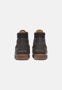 Bottes en cuir marron avec un haut de cheville, une doublure intérieure matelassée et une semelle en caoutchouc. Détails cousus et accents métalliques sur les côtés.