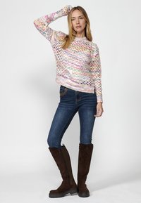 Pull en tricot avec des rayures multicolores et une laine aérée ; associé à un jean slim et des bottes en suède marron hautes avec zips latéraux.