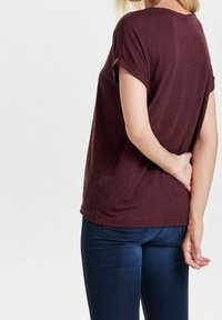 T-shirt corto bordeaux con scollo rotondo e vestibilità rilassata, abbinato a jeans blu scuro. Il tessuto sembra morbido e strutturato.