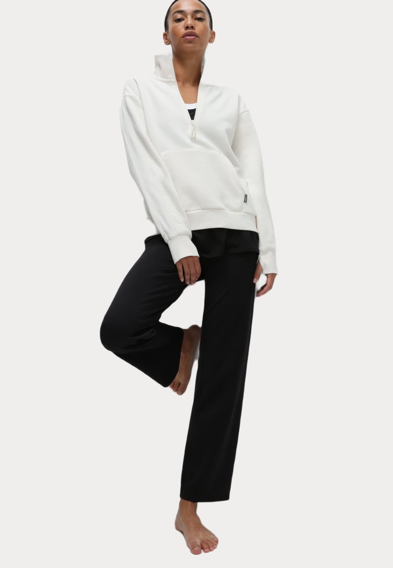 Vit zip-up sweatshirt med hög krage och framficka, i kombination med svarta vida byxor. Slät tyg, avslappnad passform, avslappnad design.