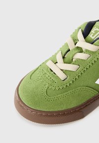 Πράσινο σουέτ αθλητικό παπούτσι με κρέμα κορδόνια, υφασμένη ραφή και σκούρο καφέ ελαστική σόλα με κανονικό σχέδιο.