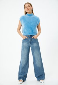 Blå fluffig ärmlös tröja med hög krage som är kombinerad med ljusblå vida jeans. Outfiten har en avslappnad passform och en casual stil.