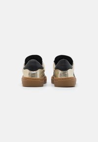Gold and black sneakers with a smooth metallic finish, featuring a textured gum rubber sole and padded black heel accents.