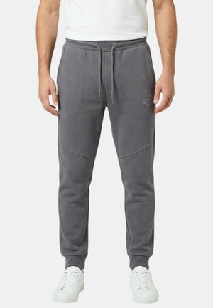Homme portant un pantalon de jogging gris à taille élastique avec cordon de serrage et poches latérales, associé à des baskets blanches et un t-shirt blanc.