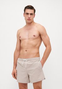 Shorts de bain beiges en tissu texturé, dotés d'une taille élastique avec cordon de serrage et de poches latérales pour le rangement.