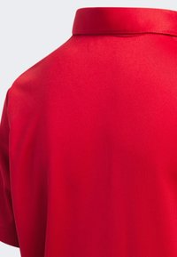 Koszulka polo z krótkim rękawem w gładkim, czerwonym materiale, z klasycznym kołnierzykiem i starannym wykończeniem. Widok z tyłu ukazuje jednorodną strukturę bez wzorów.