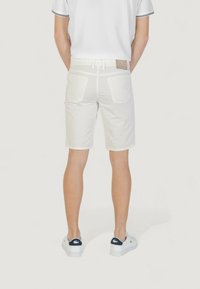 Pantalones cortos de algodón blancos con una textura suave, bolsillos traseros y un parche de cuero marrón en la cintura, combinados con zapatillas blancas.