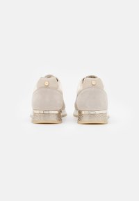 Un paio di sneakers beige e taupe con un motivo di serpente texturizzato e dettagli dorati sulla suola, viste da dietro su uno sfondo bianco.