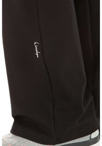 Black athletic pants made of soft fabric, featuring a slim fit and white logo near the hem. The design is simple with no patterns.