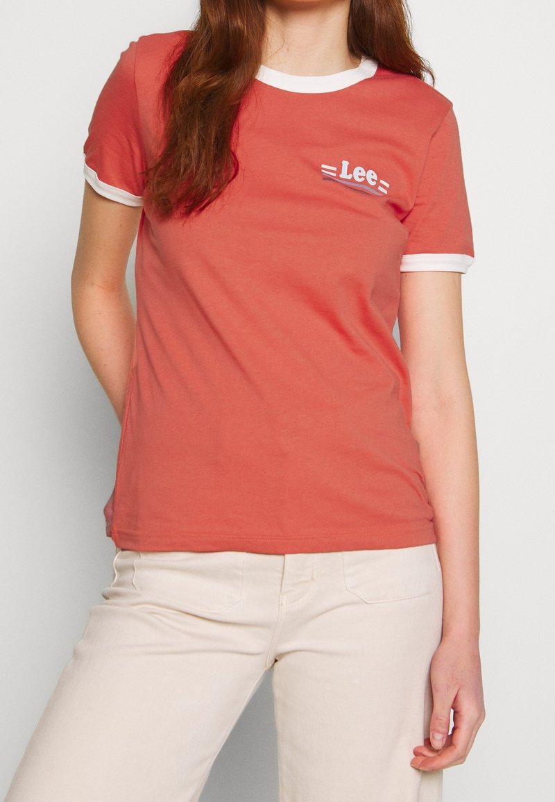 T-shirt corail avec col et manches côtelés blancs. Présente un petit logo "Lee" sur le devant. Tissu doux en coton avec une coupe ajustée.