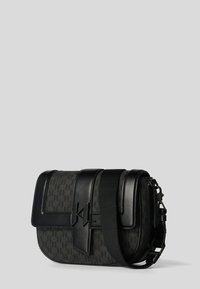 Svart axelväska med strukturert tyg och läderdetaljer. Har en lockstängning, justerbar rem och monogramdetalj på framsidan.