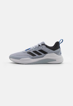 Baskets de sport gris clair avec des bandes noires, semelle blanche, languette bleue et fermeture à lacets sur fond blanc uni.