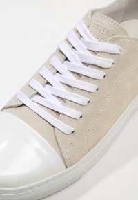 Baskets en daim beige avec embout en caoutchouc blanc, lacets blancs passés à travers six œillets, et semelle en caoutchouc blanc.