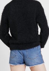 Svart fuzzy tröja med rund hals och långa ärmar, i kombination med ljusblå denimshorts med fransar och sidodetaljer.