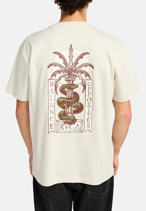 Cream cotton t-shirt featuring a graphic design with a snake and palm tree, accented by the words "BALANCE" and "OPPOSITES" in red.