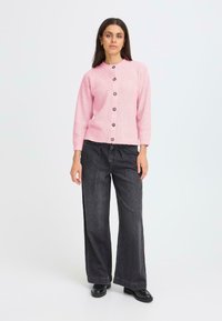 Cardigan roz cu dantelă, cu guler rotund și cinci butoane dark, asortat cu blugi negri cu talie înaltă și picioare largi, împreună cu cizme negre.