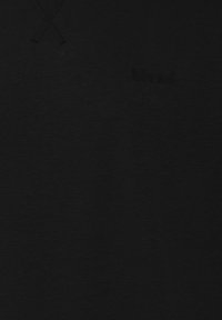 Primo piano del tessuto di un hoodie nero che mostra il sottile logo impresso "blend" e i cordini neri nella parte superiore sinistra.