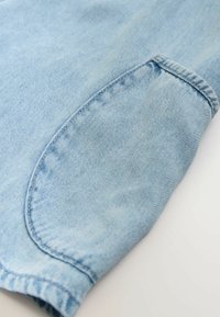 Tela de mezclilla azul clara con un bolsillo visible, mostrando una textura ligeramente desgastada y detalles de costura sutiles a lo largo de los bordes.