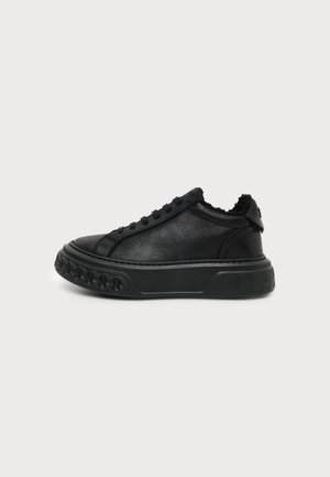 Schwarzer Low-Top-Sneaker mit strukturiertem Kettendetail auf dicker Sohle und flauschigem Innenfutter, seitlich auf hellem Hintergrund gezeigt.