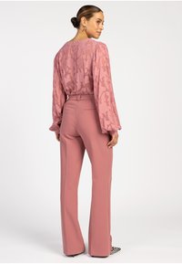 Roze kanten blouse met lange mouwen boven hoge taille roze broek, met een tekstuur van bloemenpatroon en een getailleerde silhouet, gecombineerd met gestreepte hakken.