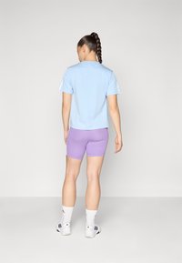 Šviesiai mėlyna trumpomis rankovėmis marškinėliai derinami su violetiniais sportiniais šortais. Apranga pasižymi laisvu pjūviu ir pralaidžia medžiaga.