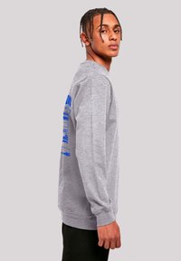 Gray long-sleeve sweatshirt featuring blue graphic text on the back, crew neck, and ribbed cuffs. Smooth texture and relaxed fit.