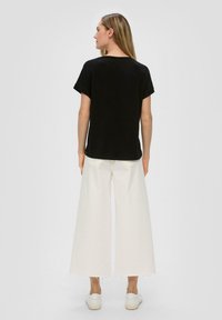 Czarna koszulka z krótkim rękawem w połączeniu z białymi spodniami o szerokich nogawkach i białymi trampkami. Ubranie ma luźny krój i minimalistyczny design.