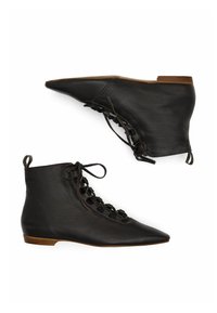 Stivali neri in pelle con punta affusolata, alla caviglia, con lacci, suole piatte marroni e linguette sul tallone, mostrati in vista laterale e della suola.