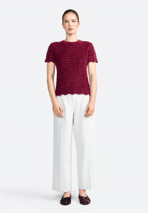 Burgundy textured knit top with a wavy design, paired with wide white striped trousers and sparkly black slip-on shoes.