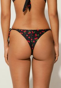 Černé bikiny s potiskem třešní, s vysoce vystřiženým designem a bočními šňůrkami. Hladká látka, minimální krytí.