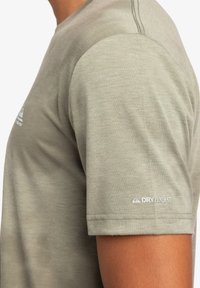 Camiseta de mangas cortas de color verde claro, hecha de una tela suave. Presenta un detalle de costura en los hombros y un logo "DRYFLIGHT" en la manga.