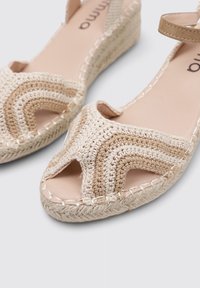 Sandalias de cuña de lino beige con diseño de punta abierta, que presentan patrones entrelazados y tela texturizada. Terminan con detalles de costura y tira en el tobillo.