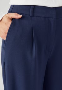 Marineblauwe broek van textuurstof, met een vlakke voorkant, zijzakken en een slank model. De tailleband is strak en op maat gemaakt.